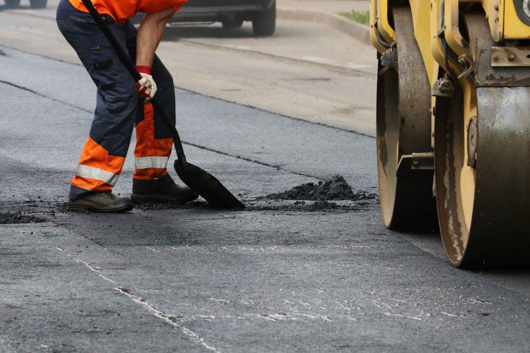 Worker using tool to smooth asphalt on driveway. Road repairing.